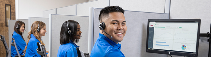 Three women and a man working in cubicles wearing headsets in front of a computer.